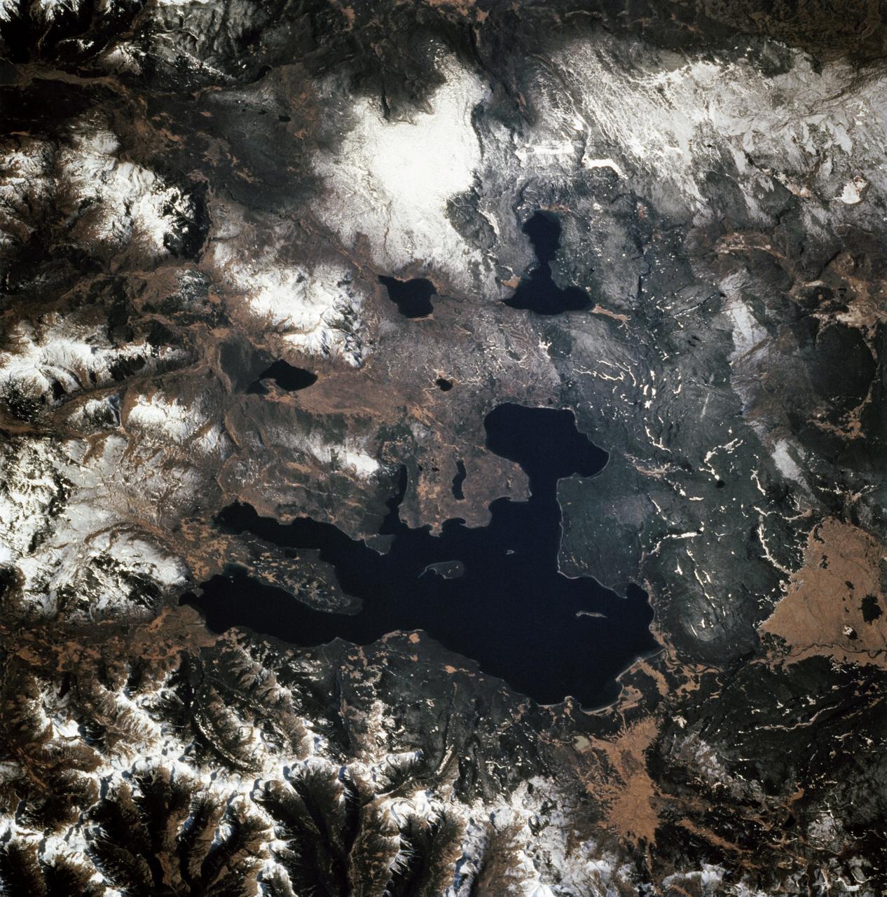 STS068-247-061 (30 September-11 October 1994) --- Photographed through the Space Shuttle Endeavour's flight windows, this 70mm frame centers on Yellowstone Lake in the Yellowstone National Park.  North will be at the top if picture is oriented with series of sun glinted creeks and river branches at top center.  The lake, at 2,320 meters (7,732 feet) above sea level, is the largest high altitude lake in North America.  East of the park part of the Absaroka Range can be traced by following its north to south line of snow capped peaks.  Jackson Lake is southeast of Yellowstone Park, and the connected Snake River can be seen in the lower left corner.  Yellowstone, established in 1872 is the world's oldest national park.  It covers an area of 9,000 kilometers (3,500 square miles), lying mainly on a broad plateau of the Rocky Mountains on the Continental Divide.  It's average altitude is 2,440 meters (8,000 feet) above sea level.  The plateau is surrounded by mountains exceeding 3,600 meters (12,000 feet) in height.  Most of the plateau was formed from once-molten lava flows, the last of which is said to have occurred 100,000 years ago.  Early volcanic activity is still evident in the region by nearly 10,000 hot springs, 200 geysers and numerous vents found throughout the park.