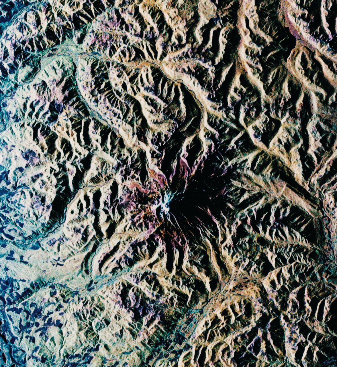 STS068-S-052 (3 October 1994) --- This is a radar image of Mount Rainier in Washington state.  The volcano last erupted about 150 years ago and numerous large floods and debris flows have originated on its slopes during the last century.  Today the volcano is heavily mantled with glaciers and snow fields.  More than 100,000 people live on young volcanic mud flows less than 10,000 years old and, are within the range of future, devastating mud slides.  This image was acquired by the Spaceborne Imaging Radar-C/X-Band Synthetic Aperture Radar (SIR-C/X-SAR) aboard the Space Shuttle Endeavour on its 20th orbit on October 1, 1994.  The area shown in the image is approximately 59 by 60 kilometers (36.5 by 37 miles).  North is toward the top left of the image, which was composed by assigning red and green colors to the L-Band, horizontally transmitted and vertically, and the L-Band, horizontally transmitted and vertically received.  Blue indicates the C-Band, horizontally transmitted and vertically received.  In addition to highlighting topographic slopes facing the Space Shuttle, SIR-C records rugged areas as brighter and smooth areas as darker.  The scene was illuminated by the Shuttle's radar from the northwest so that northwest-facing slopes are brighter and southeast-facing slopes are dark.  Forested regions are pale green in color, clear cuts and bare ground are bluish or purple; ice is dark green and white.  The round cone at the center of the image is the 14,435 feet (4,399 meters) active volcano, Mount Rainier.  On the lower slopes is a zone of rock ridges and rubble (purple to reddish) above coniferous forests (in yellow/green).  The western boundary of Mount Rainier National Park is seen as a transition from protected, old-growth forest to heavily logged private land, a mosaic of recent clear cuts (bright purple/blue) and partially re-grown timber plantations (pale blue).  The prominent river seen curving away from the mountain at the top of the image (to the northwest) is the White River, and the river leaving the mountain at the bottom right of the image (south) is the Nisqually River, which flows out of the Nisqually glacier on the mountain.  The river leaving to the left of the mountain is the Carbon River, leading west and north toward heavily populated regions near Tacoma.  The dark patch at the top right of the image is Bumping Lake.  Other dark areas seen to the right of ridges throughout the image are radar shadow zones.  Radar images can be used to study the volcanic structure and the surrounding regions with linear rock boundaries and faults.  In addition, the recovery of forested lands from natural disasters and the success of re-forestation programs can also be monitored.  Ultimately this data may be used to study the advance and retreat of glaciers and other forces of global change.  Spaceborne Imaging Radar-C/X-Band Synthetic Aperture Radar (SIR-C/X-SAR) is part of NASA's Mission to Planet Earth. (P-44703)