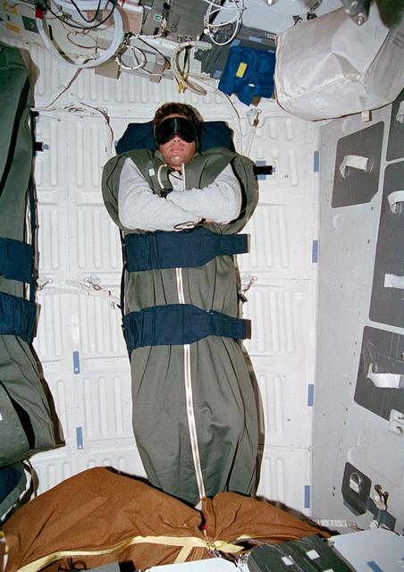 NASA image: Kregel sleeping in middeck sleep restraints wearing mask