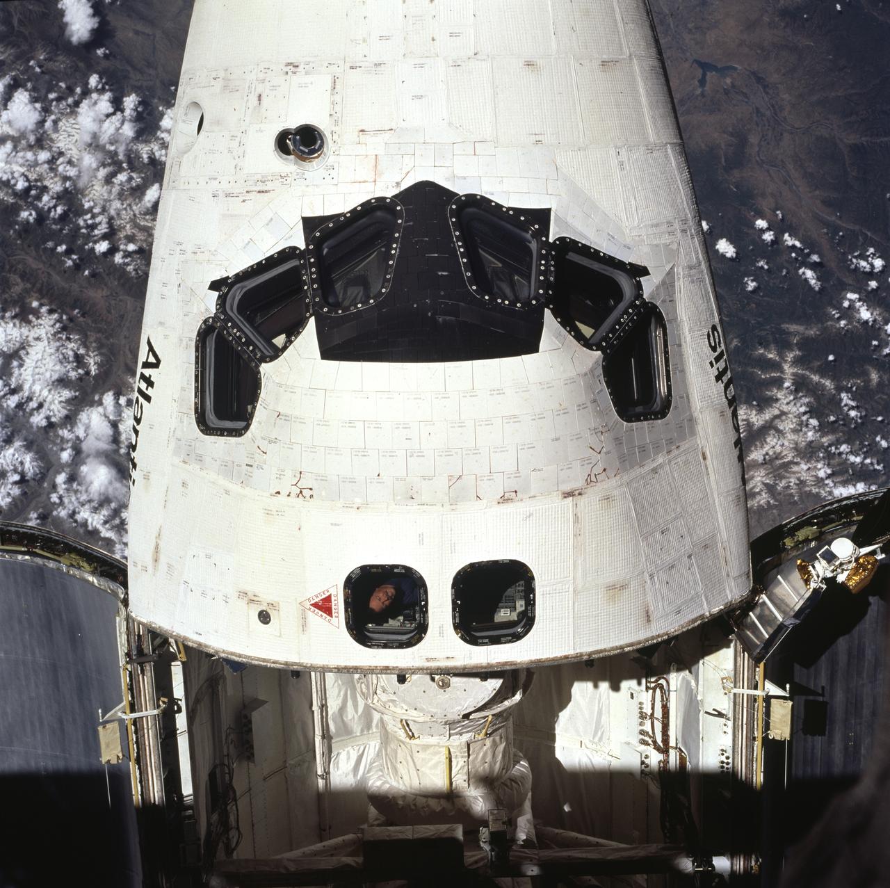 STS071-723-059 (27 June-7 July 1995) --- Docked already with Russia's Mir Space Station, the space shuttle Atlantis, with its crew cabin most prominent, is partially visible through a window on the station.  A 70mm camera, carried into space by the crew aboard Atlantis, was used to expose the image.  Above astronaut Robert L. Gibson's, STS-71 commander, head can be seen the tunnel leading to Spacelab's Science Module in Atlantis' cargo bay.  A port in the tunnel enabled the seven crew members to visit Mir and it allowed the three Mir-18 crewmembers, in space since March of this year, access to Spacelab.  That module was quite busy with tests and data collection involving the three until Atlantis brought them home on July 7, 1995.