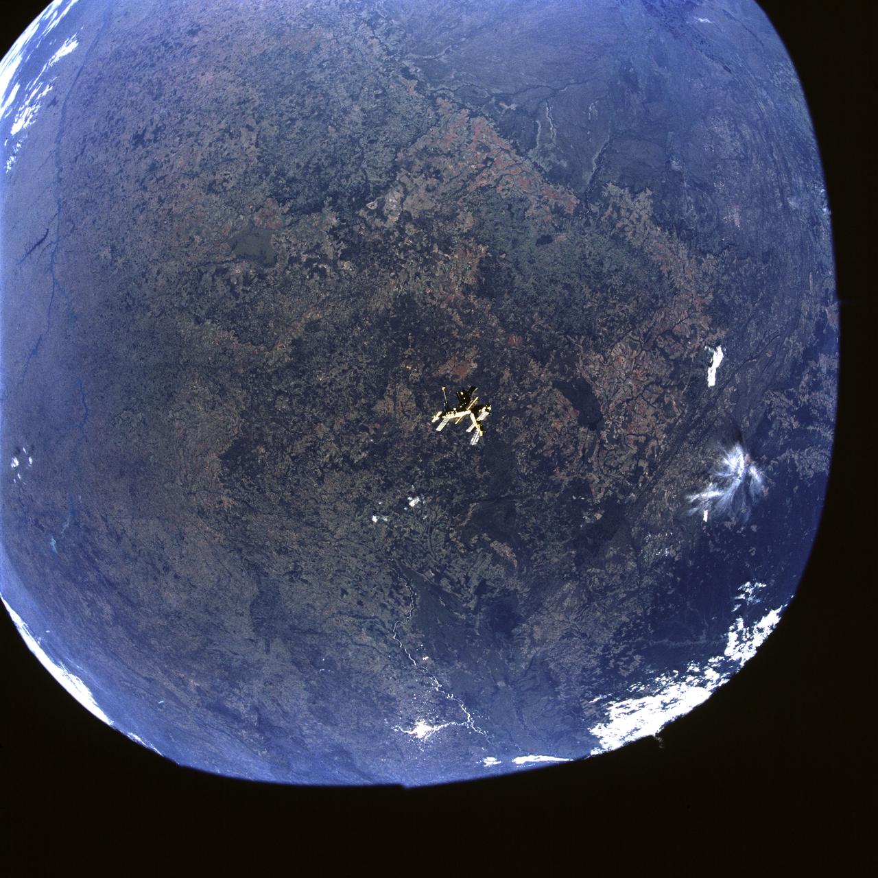 STS071-741-091 (27 June-7 July 1995) --- This wide-angle view shows Russia's Mir Space Station backdropped against much of south-central Brazil (an area of more than 600 miles is represented from left edge to right). The area covers from the rainforest of Amazonia at top left, to the undeveloped swamplands of the Pantanal at bottom left in a lighter shade of green, to the Parana, running southward to Argentina down the right side of the view. Brown colors all around Mir indicate agricultural lands: brown and red colors are the colors of tropical soils which underlie the region and are visible because some soils have been exposed by plowing. Brasilia, the capital district of Brazil, is not visible in this view but lies near the light blue lake top right in the headwaters of the Parana River.