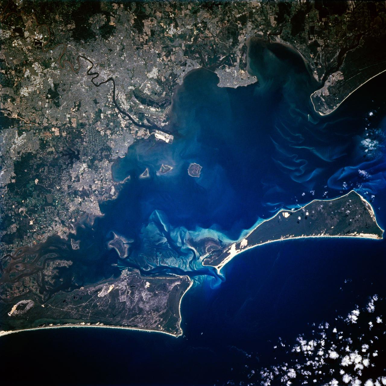 STS072-721-010 (11-20 Jan. 1996) --- Astronauts aboard the Space Shuttle Endeavour exposed this frame of Brisbane, the third largest city in Australia, as well as the capital of Queensland. The heart of the city is 12 miles from Moreton bay and is located on the Brisbane River. In the photograph this area is clearly visible due to the "W"-shaped bend in the river. Mount Coot-Na Park is the dark area on the upper edge of the frame. This area provides an overlook for the entire city. Moreton Island is the Exclamation shaped island protecting the harbor. Fraser Island is about 150 miles north of Brisbane. The international airport is directly above the river in this view.