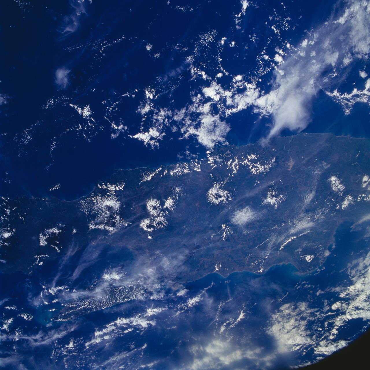 STS072-737-012 (11-20 Jan. 1996) --- The astronauts photographed this view of Java, an Indonesian island.  Java lies between the Java Sea at top and the Indian Ocean at bottom (north is located at top center).  A line of volcanoes on the southern edge of the island, trending from central to eastern areas, is highlighted by a ring of clouds.  Off the southern coast of Java is the Java Trench where the Australian plate, to the south, is diving under the Eurasia plate to the north.  According to anthropologists, Java has one of the highest populations in Indonesia because the soil is enriched by volcanic ash.  Merapi volcano, at left edge, second volcano to the right, rises to 9,550 feet and erupts frequently.  Madura Island, partially obscured by clouds, can be seen on the upper eastern end of Java.