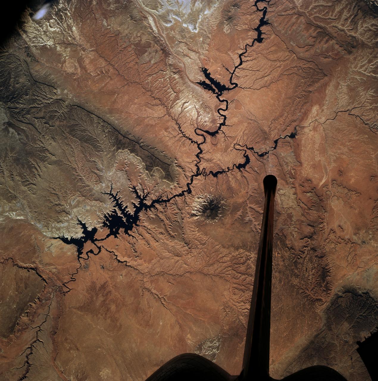 STS073-727-045 (21 October 1995) --- Photographed by the astronauts aboard the Space Shuttle Columbia is this scene over Lake Powell. The lake was formed by the Glen Canyon Dam on the Colorado River. The vertical stabilizer of Columbia points northeastward. Navaho Mountain, northwest of the tail, according to NASA geologists, was formed by an intrusion of molten rock that uplifted older, layered rocks, then cooled, and has been exposed by erosion. The rest of the landscape is dominated by faulted layers of sandstone, shale, and limestone that were formed in shallow seas and great deserts 80 to 250 million years ago. These rocks of the Colorado Plateau were uplifted a few million years ago to be dissected by the meandering Colorado River, San Juan River, and their tributaries.