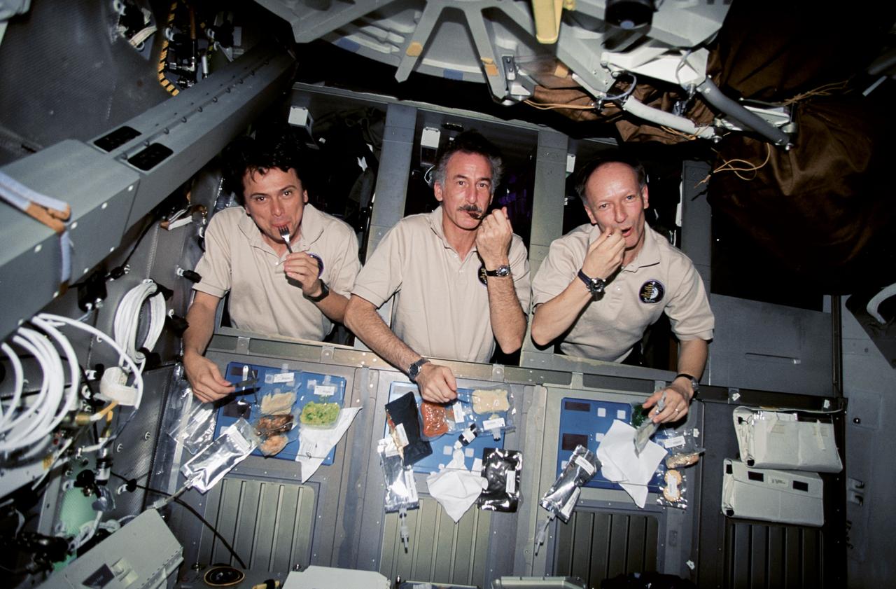 STS075-302-016 (22 Feb.-9 March 1996) --- Soon after reaching Earth orbit, the blue shift team set up what they referred to as a "formal" meal on the space shuttle Columbia's middeck. Left to right are astronauts Franklin R. Chang-Diaz, STS-75 payload commander; Jeffrey A. Hoffman and Claude Nicollier, both mission specialists. Hoffman later told a gathering of Johnson Space Center employees that the meal was accompanied by classical music. Photo credit: NASA or National Aeronautics and Space Administration