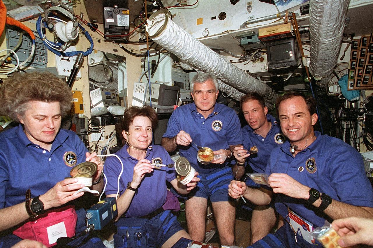 STS076-345-028 (22 - 31 March 1996) --- Onboard the Base Block Module of Russia's Mir Space Station the visiting STS-76 crew members enjoy Russian food.  At right is astronaut Kevin P. Chilton, mission commander, who along with his crew mates docked with Mir on March 23, 1996, and remained linked until March 28, 1996.  Left to right are astronauts Shannon W. Lucid, Linda M. Godwin and Michael R. (Rich) Clifford, all mission specialists, along with Richard A. Searfoss, pilot.  The right hand of payload commander Ronald M. Sega is at right edge.  Lucid was in the process of transferring from STS-76 to the Mir-21 crew, which thereby grew from two to three members.  Lucid will remain aboard Mir for approximately 140 days, as a cosmonaut guest researcher.