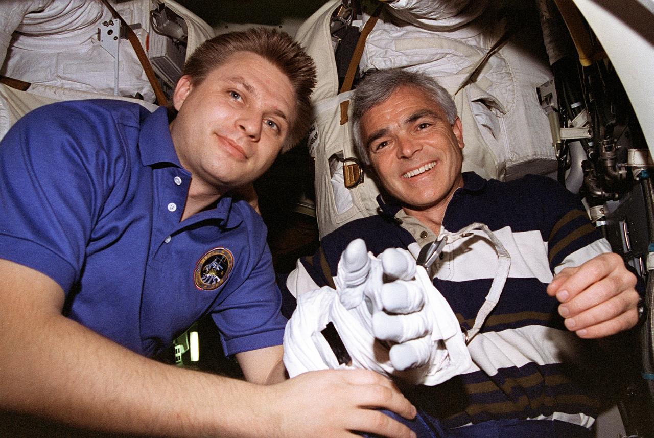 STS076-356-006 (26 March 1996) --- Backdropped against two space suits, a curious cosmonaut Yury I. Onufrienko, left, tries on a glove while visiting astronaut Michael R. (Rich) Clifford in the airlock aboard the Space Shuttle Atlantis.  Clifford was in the airlock to check over his gear for tomorrow's Extravehicular Activity (EVA).  Onufrienko is Mir-21 mission commander, and Clifford, a STS-76 mission specialist who will be joined by astronaut Linda M. Godwin for the EVA.  The EVA of the two mission specialists marks the first EVA while Russia's Mir Space Station was docked with the Space Shuttle Atlantis.  This is the third of a series of docking missions involving Mir and the Space Shuttle Atlantis.
