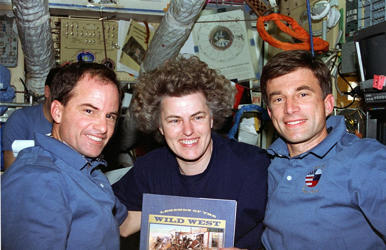 STS076-356-029 (22 - 31 March 1996) --- Astronaut Shannon W. Lucid, cosmonaut guest researcher, shows off a book which will occupy some of her off-duty time and that of her two Mir-21 crew mates aboard Russia's Mir Space Station during the next five months.  Lucid was about to bid farewell to STS-76 crew mates Kevin P. Chilton (left), mission commander, and Ronald M. Sega, payload commander.  The book was a gift from the STS-76 crew, given to the Mir-21 crew.  This photograph was made onboard Mir's Base Block Module.  After leaving Lucid to her duties onboard Mir, Chilton, Sega and three other astronauts later returned to Earth aboard the Space Shuttle Atlantis.