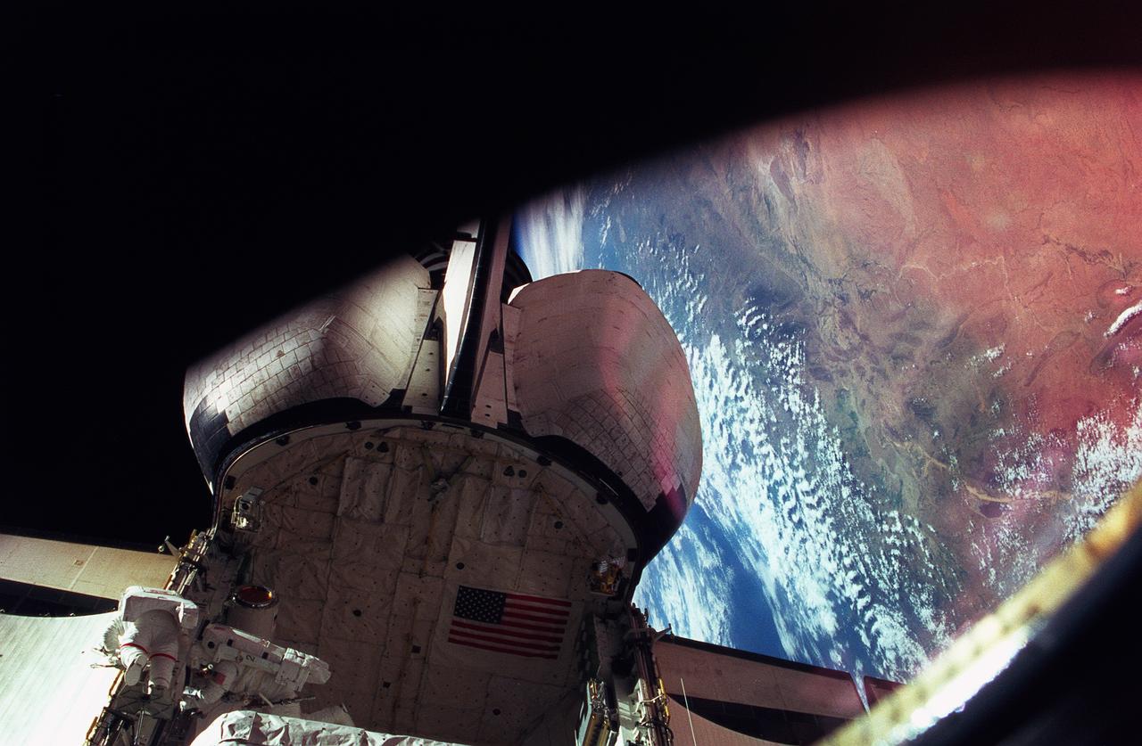 STS076-401-021 (27 March 1996) --- Astronauts Michael R. (Rich) Clifford (right) and Linda M. Godwin (red stripe) work together on the port side of the Space Shuttle Atlantis' aft cargo bay during a March 27, 1996, Extravehicular Activity (EVA).  The Atlas Mountains can been seen near Earth's horizon in the background.  The EVA of the two mission specialists marks the first EVA while Russia's Mir Space Station was docked with the Space Shuttle Atlantis.  This is the third of a series of docking missions involving Mir and the Space Shuttle Atlantis.