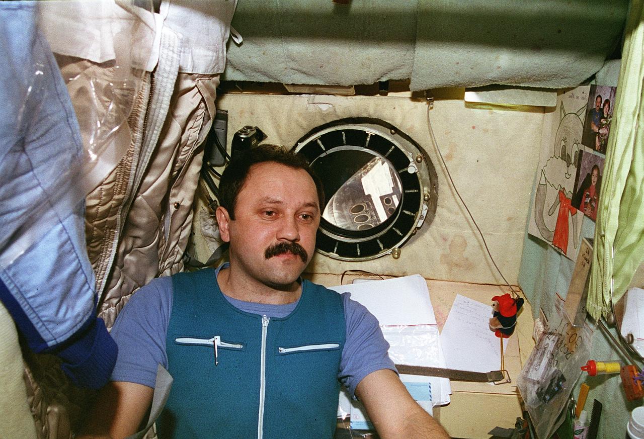 STS076-461-014 (22-31 March 1996) --- Cosmonaut Yury V. Usachev, Mir-21 flight engineer, reflects on his mission duties in his living quarters aboard Russia's Mir Space Station.  His temporary out-the-window scenery is provided by the nose of the Space Shuttle Atlantis, which docked with Mir on March 23, 1996.