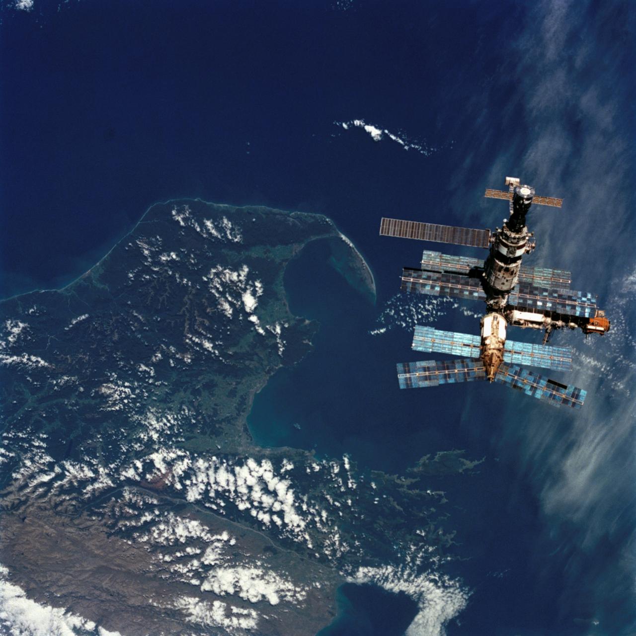 STS076-713-036 (23 March 1996) --- Backdropped against the waters of Cook Strait near New Zealand's South Island, Russia's Mir Space Station is seen from the aft flight deck window of the Space Shuttle Atlantis.  The two spacecraft were in the process of making their third docking in Earth-orbit.  With the subsequent delivery of astronaut Shannon W. Lucid to the Mir, the Mir-21 crew grew to three, as the mission specialist quickly becomes a cosmonaut guest researcher.  She will spend approximately 140 days on Mir before returning to Earth.