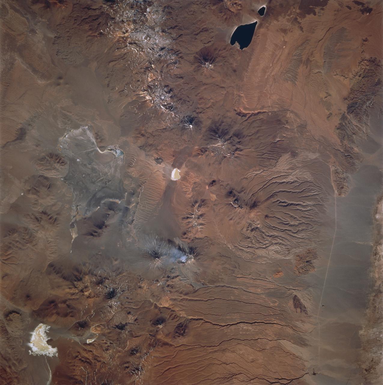 STS077-740-029 (19-29 May 1996) --- In recent years, the most active peak in the High Altiplano of the central Andes Mountains has been Lascar, in northern Chile - featured in this 70mm frame.  North is to the left in this picture.  Lascar?s largest recent eruption was in April, 1993.  The STS-55 crew photographed large dust plumes carrying the newly-deposited ash about one week after the eruption.  Since then, astronauts have been closely monitoring Lascar, which remains active.  This crew noticed and photographed Lascar?s plume, which is shown here as a steam plume rising from Lascar?s central summit crater.  This level of activity is typical.  This view also shows the extent of weathering as determined by the surface color of the 1993 flow from the crater.  The flow traveled down the valley which is to the left (north) and then down (west) from the summit of this image.  In earlier views the flow was a light gray, almost white feature in the valley.  Today, the flow is close to the red-brown color of the surrounding rock.