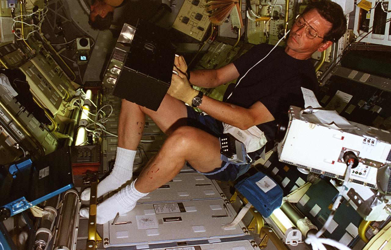 STS078-301-021 (20 June - 7 July 1996) --- Payload specialist Jean-Jacques Favier, representing the French Space Agency (CNES), holds up a test container to a Spacelab camera. The test involves the Bubble Drop Particle Unit (BDPU), which Favier is showing to ground controllers at the Marshall Space Flight Center (MSFC) in order to check the condition of the unit prior to heating in the BDPU facility. The test container holds experimental fluid and allows experiment observation through optical windows. BDPU contains three internal cameras that are used to continuously downlink BDPU activity so that behavior of the bubbles can be monitored. Astronaut Richard M. Linnehan, mission specialist, conducts biomedical testing in the background.