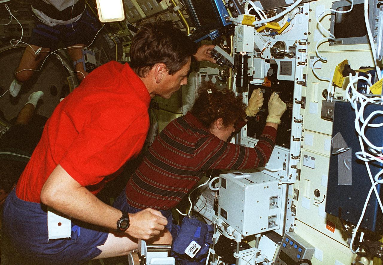 STS078-306-035 (20 June - 7 July 1996) --- Astronaut Susan J. Helms, payload commander, and payload specialist Jean-Jacques Favier, representing the French Space Agency (CNES), insert a test container into the Bubble Drop Particle Unit (BDPU) in the Life and Microgravity Spacelab (LMS-1) Science Module aboard the Space Shuttle Columbia. The fluid in the chamber is heated and the fluid processes are observed by use of three internal cameras mounted inside the BDPU. Investigations in this facility will help characterize interfacial processes involving either bubbles, drops, liquid columns or liquid layers.