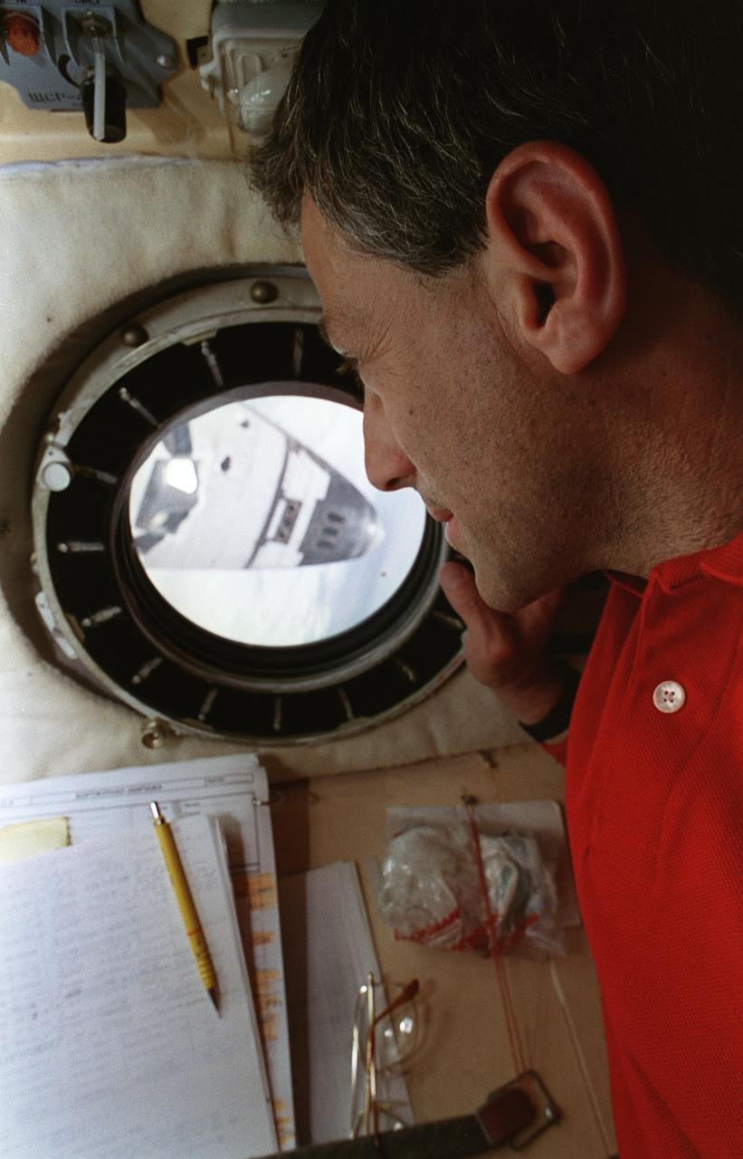 STS079-335-025 (16-26 Sept. 1996) --- Astronaut Jerome (Jay) Apt, in the flight engineer's cabin aboard Russia's Mir Space Station, appears nose to nose with the space shuttle Atlantis as he peers through a viewing port at the forward section of the Orbiter while the two spacecraft were docked in Earth-orbit.