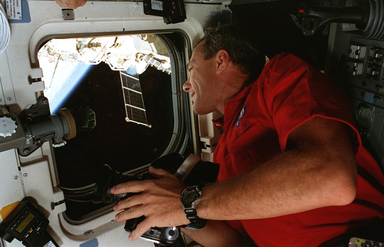 STS079-353-007 (16-26 Sept. 1996) --- Astronaut Terrence W. Wilcutt, on the Space Shuttle Atlantis' aft flight deck, takes pictures of Earth for study by Earth observations scientists at the Johnson Space Center (JSC).  Several components of the docked Russia's Mir Space Station can be seen in the background.  This photograph is one of fifteen 35mm frames (along with four 70mm frames) of still photography documenting the activities of NASA's STS-79 mission, which began with a September 16, 1996, liftoff from Launch Pad 39A the Kennedy Space Center (KSC) and ended with a landing at KSC on September 26, 1996.  Onboard for the launch were astronauts William F. Readdy, commander; Wilcutt, pilot; John E. Blaha, Jerome (Jay) Apt, Thomas D. Akers and Carl E. Walz, all mission specialists.  On flight day 4, the crew docked with Russia's Mir Space Station.  Shannon W. Lucid, who had spent six months aboard Mir, switched cosmonaut guest researcher roles with Blaha.  The latter joined fellow Mir-22 crew members Valeri G. Korzun, commander, and Aleksandr Y. Kaleri, flight engineer.