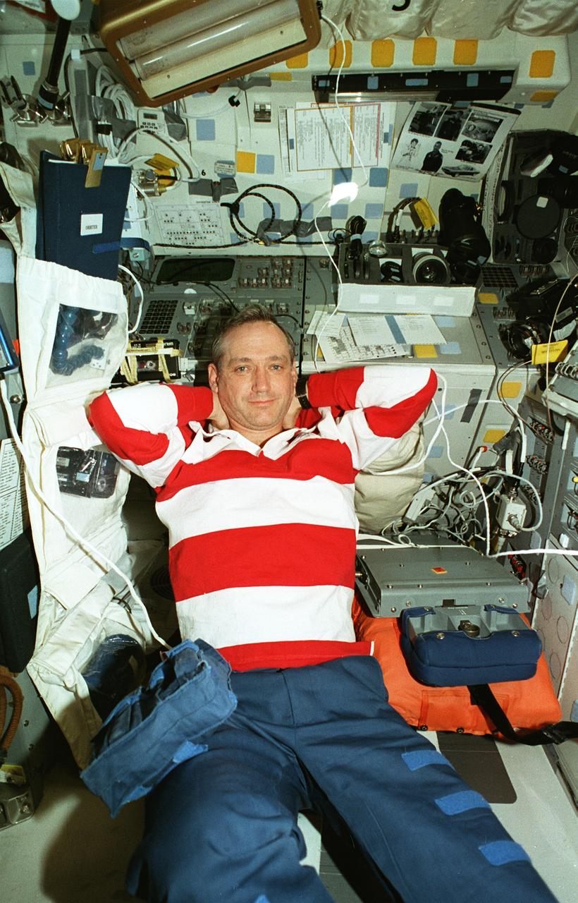 STS079-354-016 (20 Sept. 1996) --- Astronaut Thomas D. Akers, mission specialist, spends a few moments of his off-duty time aboard the Space Shuttle Atlantis in a rare relaxed posture.  Akers is on the aft flight deck, looking toward overhead windows (out of frame) through which he could see several of the components of Russia's Mir Space Station, docked for several days to Atlantis.  Later, during a post-flight presentation to an assembly of co-workers in Houston, astronaut William F. Readdy, mission commander, recalled this moment as the only one on the STS-79 flight during which he witnessed Akers not busy with transfer chores or Spacehab experiment tasks.  Several pieces of camera equipment and a stowed chair used during launch and entry are identifiable among the items on the flight deck.