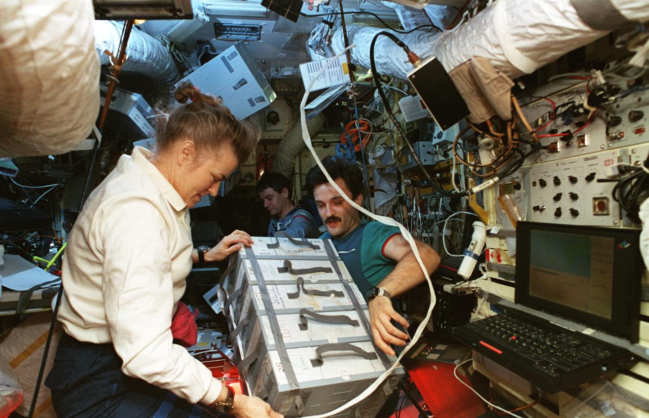STS079-357-015 (20 Sept. 1996) --- Astronaut Shannon W. Lucid, in one her final opportunities to work with cosmonauts on her record stay in space, joins cosmonaut Aleksandr Kaleri in securing empty food trays to be moved from Russia's Mir Space Station to the Space Shuttle Atlantis.  Cosmonaut Valeri Korzun, Mir-22 commander, is busy with other chores in the background.