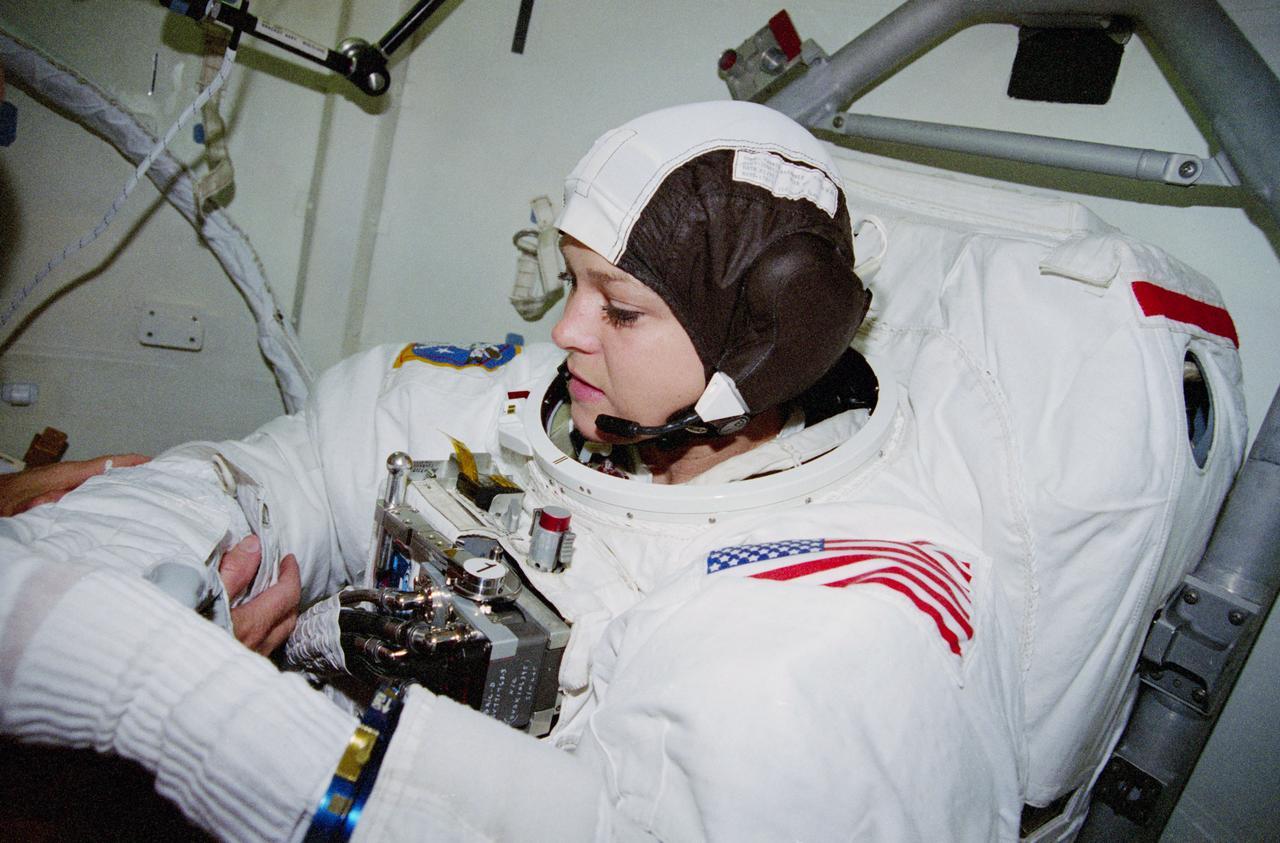 STS080-312-027 (28 Nov. 1996) --- Astronaut Tamara E. Jernigan uses the assistance of astronaut Story Musgrave (out of frame, left) during suit donning for a scheduled Extravehicular Activity (EVA). Unfortunately, the EVA was canceled after the astronauts were unable to open the Space Shuttle Columbia's hatch leading to the cargo bay.