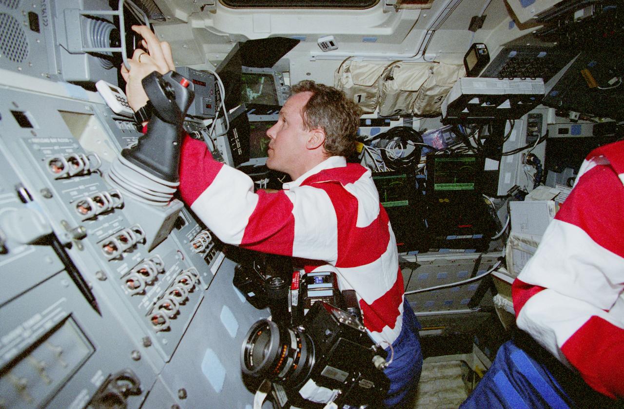 STS080-330-023 (19 Nov.-7 Dec. 1996) --- Astronaut Thomas D. Jones, STS-80 mission specialist, operates the Remote Manipulator System (RMS) controls during operations with the Wake Shield Facility (WSF). When this picture was taken, the part time free-flying WSF was in the grasp of the RMS' end effector, as evidenced by the scene on the space shuttle Columbia's aft flight deck monitor in upper right.