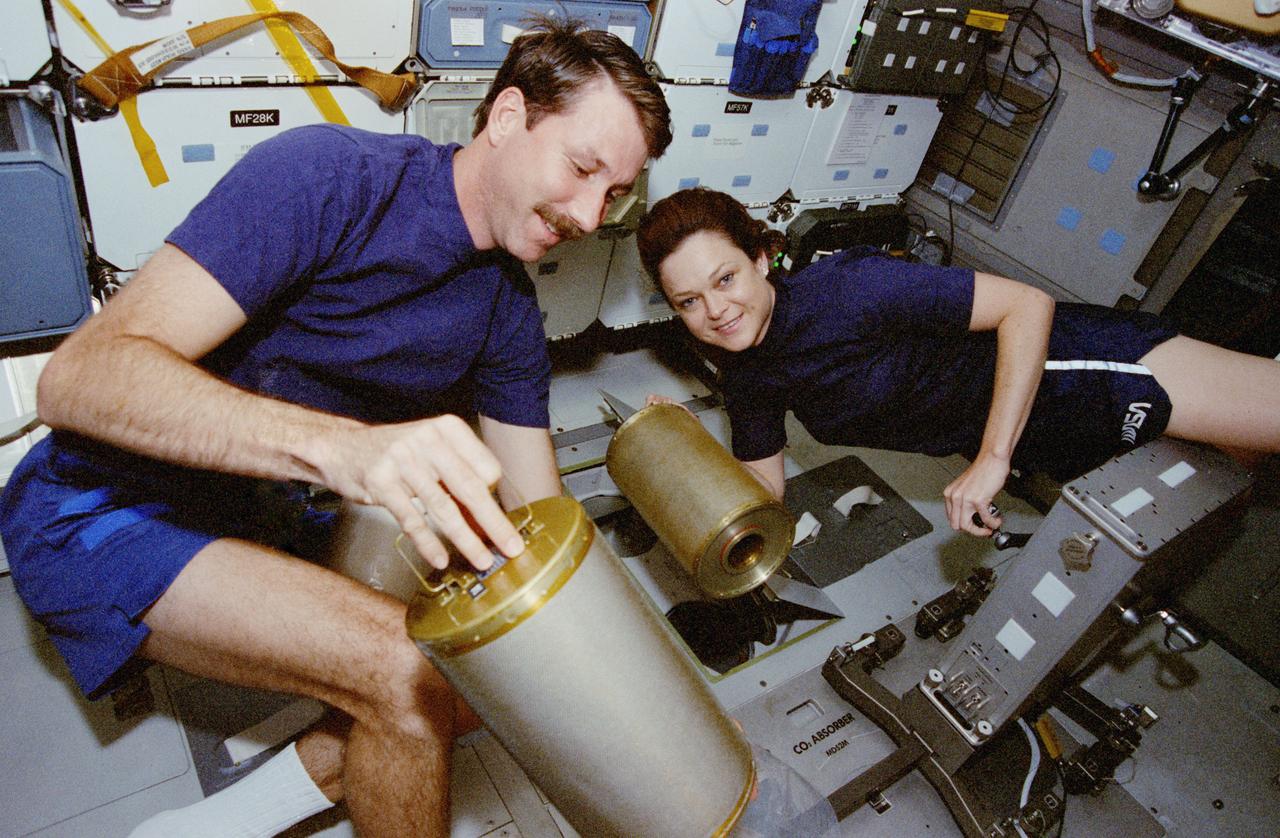 STS080-331-030 (19 Nov.-7 Dec. 1996) --- Astronauts Kent V. Rominger, STS-80 pilot, and Tamara E. Jernigan, mission specialist, perform a routine housekeeping chore during the space shuttle Columbia's record stay in Earth-orbit. The two are changing out the lithium hydroxide canisters beneath the middeck.