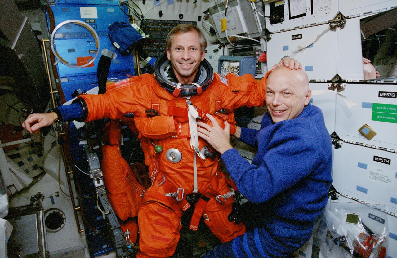 STS080-375-029 (6 Dec. 1996) --- On the middeck of the Earth-orbiting space shuttle Columbia, astronaut Story Musgrave helps with the final touches of suit donning for astronaut Kenneth D. Cockrell, STS-80 mission commander. The orange suit is a partial pressure launch and entry garment. The crew, initially waved off from its scheduled landing, eventually brought the Columbia home on Dec. 7, 1996.