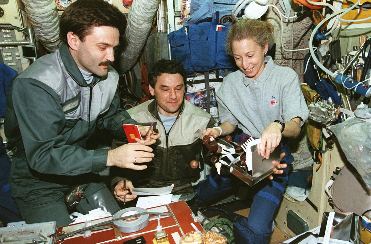 STS081-369-020 (12-22 Jan. 1997) --- Astronaut Marsha S. Ivins and two Mir-22 crewmembers stray from the conventional food fare as they open a box of chocolates on Russia's Mir Space Station's Base Block Module.  Cosmonauts Aleksandr Y. Kaleri (left), flight engineer, and Valeri G. Korzun, share the treats.