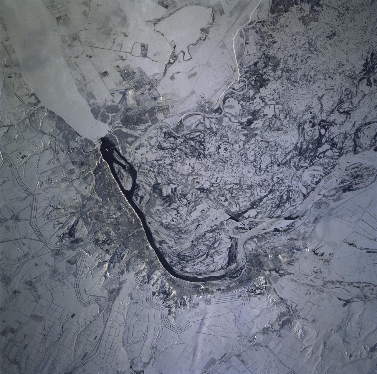 STS081-715-004 (12-22 Jan. 1997) --- As photographed with a 70mm camera aboard the Space Shuttle Atlantis, this scene features the Volga River and Volgograd under snow. Contrast in brightness shows up many features in this near-vertical view of the great bend of the Volga River's dark, open strip of water, center. The Volga flows south into the view from top right, then southeast from the center to the bottom. Volgograd appears as the gray zone along the left (west) side of the open water. Presumably the ice-free part of the river opposite Volgograd relates to the slightly warmer water which is spilled from prominent, ice-covered Lake Volgograd (top right). The wide patterns of swirls, center to lower right, are numerous meander bends on the Volga's floodplain (up to 20 miles wide), highlighted by snow. The main course of the Volga is once again ice covered in this floodplain belt. The Volga-Don Canal can be seen leaving the river just south of the bend, exiting the view center left. This canal, with others in the Moscow region, allows barge traffic to move through the Russian heartland, from the Black Sea to the Baltic at Leningrad. The long parallel lines in threes and fours are lines of trees used as wind breaks. They stretch across Russia for hundreds of miles.