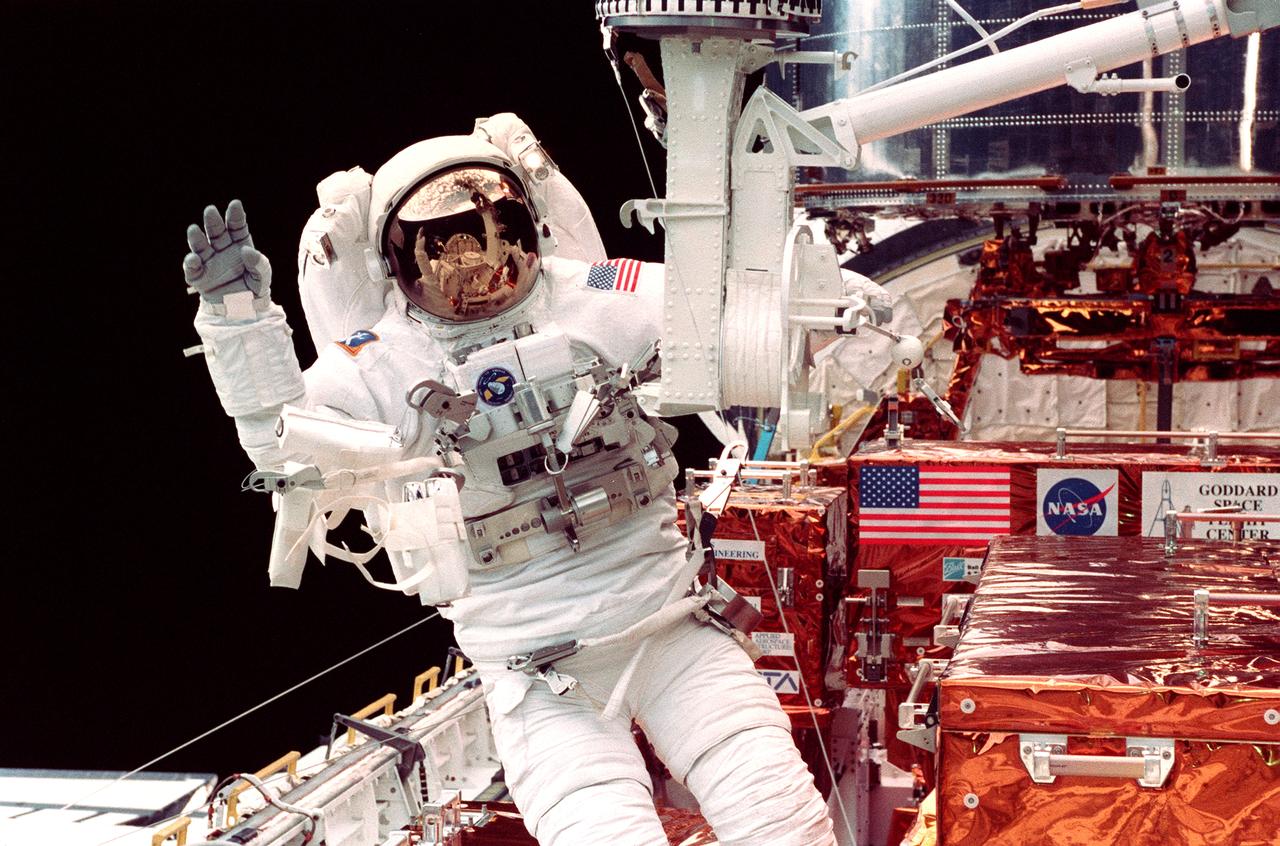 STS082-339-035 (15 Feb. 1997) --- Astronaut Steven L. Smith waves at in-cabin crewmates while working near the foot restraint of the Remote Manipulator System (RMS) during the third day of extravehicular activity (EVA-3) to service the Hubble Space Telescope (HST).  Astronaut Mark C. Lee, payload commander who shared walk chores with Smith, is out of frame.