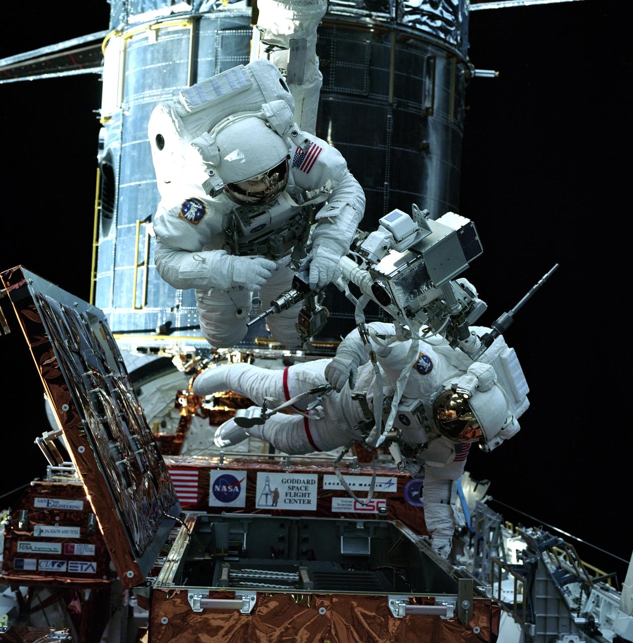STS082-717-026 (13 Feb. 1997) --- Gearing up with tools for the first Extravehicular Activity (EVA-1) to service the Hubble Space Telescope (HST, background) are astronauts Steven L. Smith (left) and Mark C. Lee. They were among four STS-82 crewmembers who are to share several alternating two-member space walking work sessions during the flight. The photograph was made from inside Discovery's cabin with a 70mm camera.