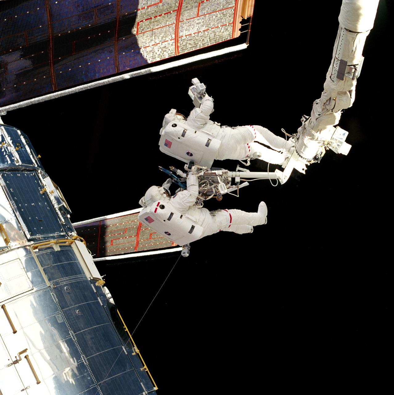STS082-719-002 (14 Feb. 1997) --- Astronaut Joseph R. Tanner (right) stands on the end of Discovery's Remote Manipulator System (RMS) arm and aims a camera at the solar array panels on the Hubble Space Telescope (HST) as astronaut Gregory J. Harbaugh assists. The second Extravehicular Activity (EVA) photograph was taken with a 70mm camera from inside Discovery's cabin.