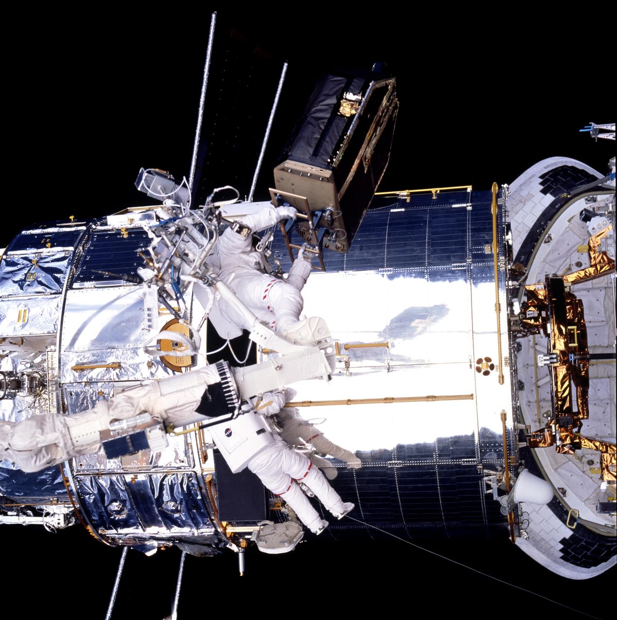 STS082-742-047 (11-21 Feb. 1997) --- On Flight Day 5, astronaut Joseph R. Tanner (left) holds a 500 pound piece of hardware as he stands on the end of the Space Shuttle Discovery's Remote Manipulator System (RMS) arm, as tethered astronaut Gregory J. Harbaugh works nearby.  The piano-shaped object held aloft by Tanner is actually the Fine Guidance Sensor 1 (FGS-1), which Tanner had just removed from the Hubble Space Telescope (HST).  Harbaugh is inspecting the FGS' bay to set the stage for the two to insert the replacement hardware.    EDITOR'S NOTE:  For orientation purposes, the picture should be held with Space Shuttle's OMS pods at top.