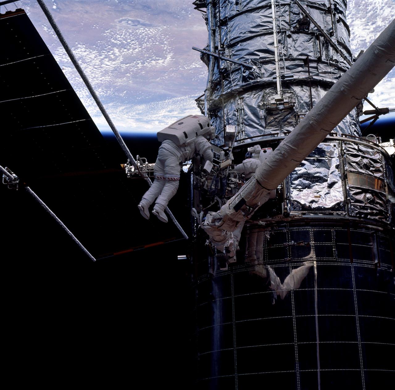 STS082-744-060 (11-21 Feb. 1997) --- Astronauts Joseph R. Tanner (left-with red and white stripes) and Gregory J. Harbaugh (partially obscured) team up to replace the Solar Drive Electronics (SADE) on the temporarily captured Hubble Space Telescope (HST) in the Space Shuttle Discovery's cargo bay.  The Extravehicular Activity (EVA) took place on Flight Day 7, during the fourth of five total EVA's utilized to service HST.
