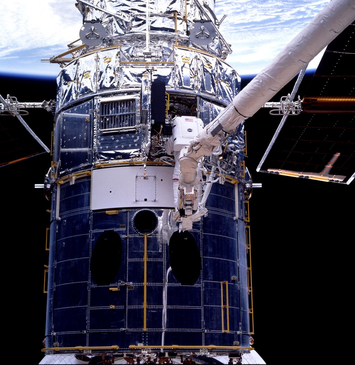 STS082-752-020 (11-21 Feb. 1997) --- Astronaut Mark C. Lee, standing on the end of the Remote Manipulator System (RMS), works at the data interface unit on the Hubble Space Telescope (HST), temporarily captured in the cargo bay of the Earth-orbiting the Space Shuttle Discovery. This third space walk or Extravehicular Activity (EVA) of the mission took place on Flight Day 6, with astronauts Lee, payload commander, and Steven L. Smith, mission specialist, serving as the suited EVA participants.