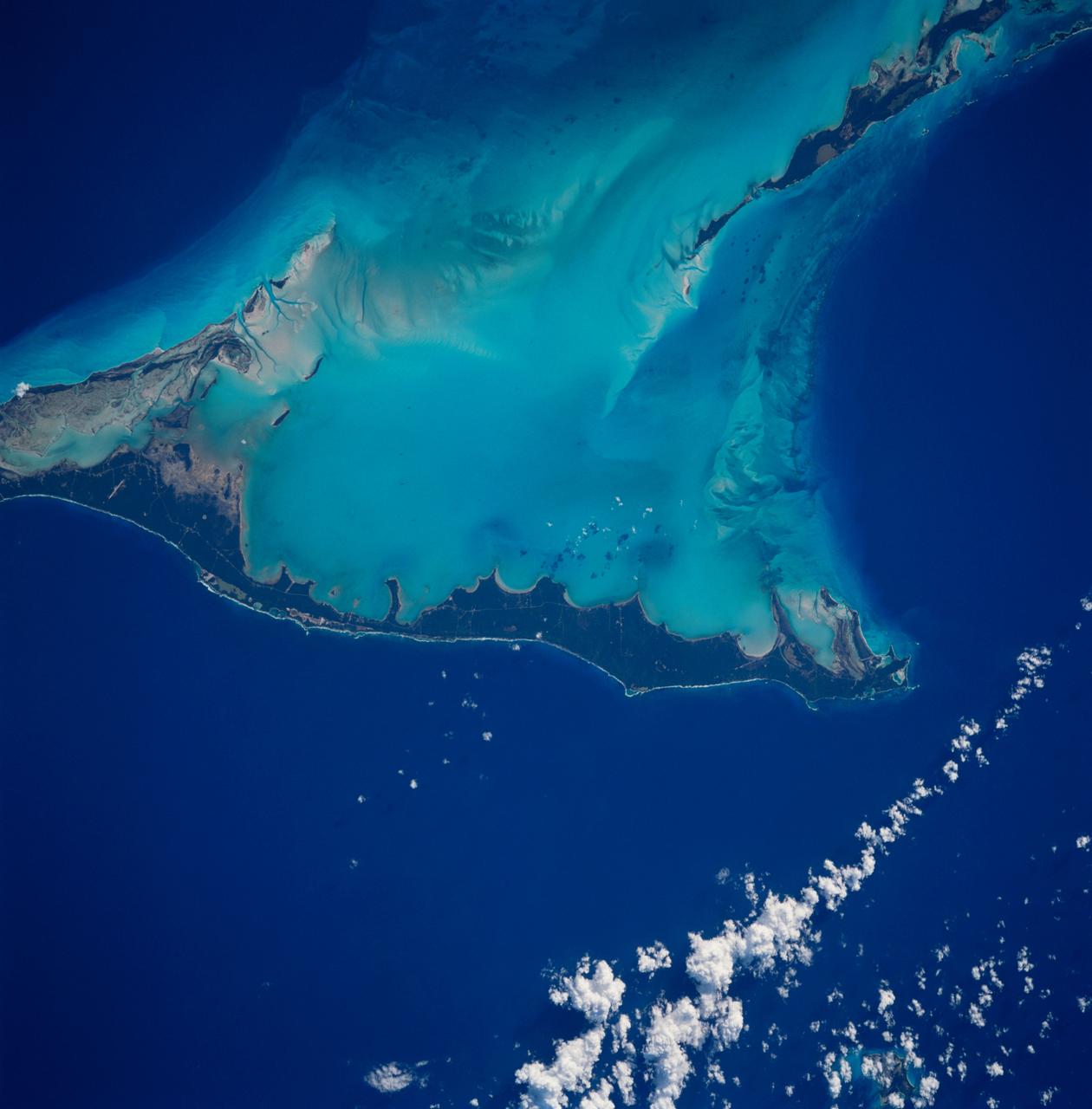 STS083-712-063 (4-8 April 1997) --- Northern half of Long Island, Bahamas.  The vivid blues of the Bahamas stand out from space.  Long Island and Great Exuma Island, which extends from the west north west into the photo, is on the eastern side of the Great Bahama Bank and form the borders of Exuma Sound.  This photograph provides a rare opportunity to observe a natural chemical laboratory at work.  Limestone of quite a different sort from that forming the Great Barrier Reef is actually in the process of formation.  Long Island itself is little more than a sandbar rising just a few meters (about 30 to 50 meters) above sea level but it separates the deep, dark blue waters of the Atlantic on the right from the 10-meter (33 feet) shallows of the Great Bahama Bank (left).  Details of the topography of the bank are visible through the clear waters.  The shallow waters are warm and become extremely salty.  Crystals of aragonite, a calcium carbonate mineral, are precipitated and formed into spherical sand-sized oolites as the tidal currents swirl back and forth.  Lithification of the carbonate sands produces an oolithic limestone.  Although the water is warm and clear, corals do not live in the shallows, probably because of the elevated salt content.  Although chemically similar, the oolithic limestone forming Long Island is very different from coral reef limestone.  An airfield is visible at the northern and central (bottom of photo) part of the island.