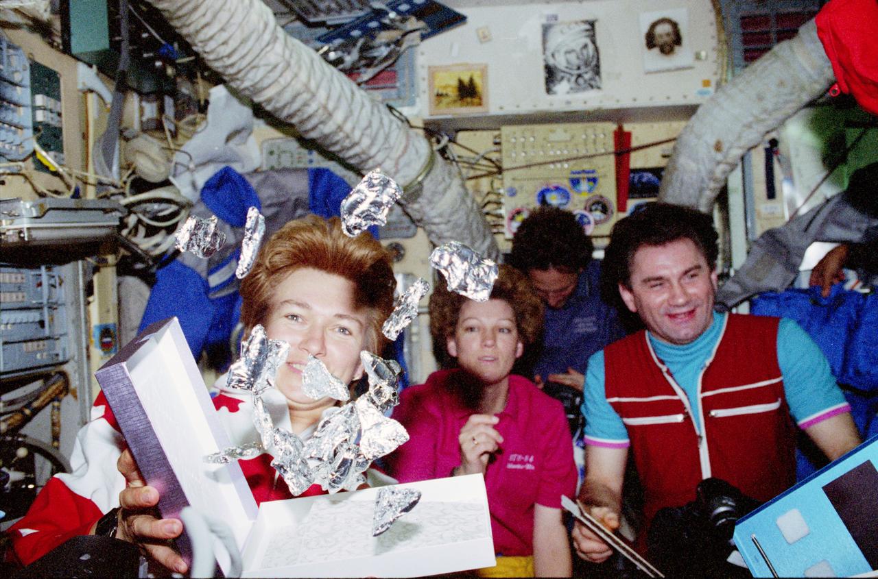 STS084-377-026 (15-24 May 1997) --- Cosmonaut Elena V. Kondakova opens a gift box and a number of tiny chocolate Space Shuttles free-float in Russia's Mir Space Station's Base Block. The STS-84 mission specialist and her crew mates had earlier presented the gift to the Mir-23 crew members, including Vasili Tsibliyev (right), mission commander. In the background are astronauts Eileen M. Collins, STS-84 pilot, and Jerry M. Linenger, mission specialist. Linenger was in his last days aboard Mir prior to returning to Earth with the STS-84 crew aboard the Space Shuttle Atlantis.