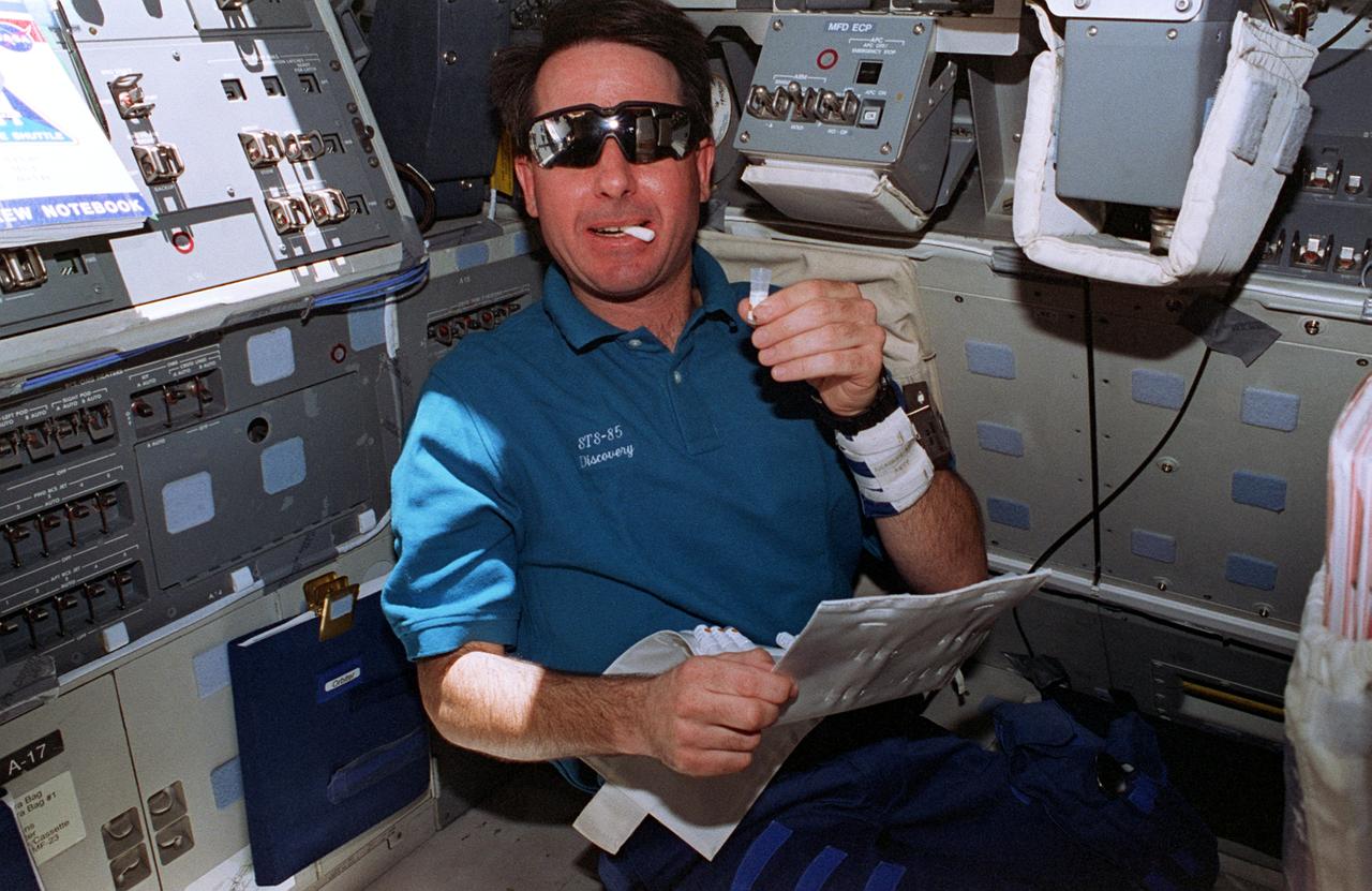 STS085-338-016 (7 - 19 August 1997) --- On the Space Shuttle Discovery's flight deck, astronaut Stephen K. Robinson conducts one phase of the mission's Detailed Supplementary Objectives (DSO). He uses a cotton swab to collect a saliva sample. The wrist band on his left arm is associated with the same DSO. The ongoing test, dealing with circadian rhythm and other biological systems, is in preparation for the International Space Station (ISS).