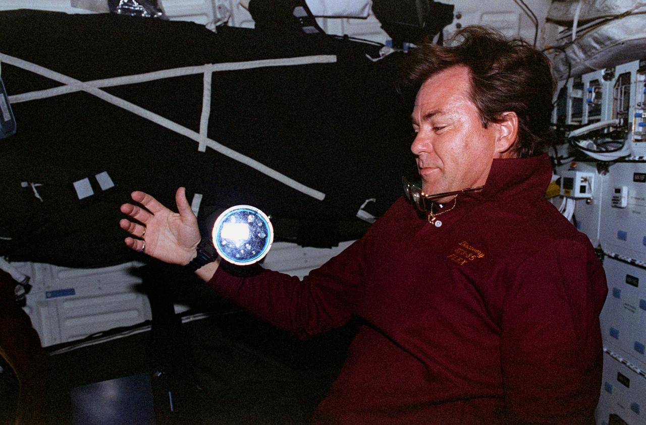 STS085-351-003 (7 - 19 August 1997) --- Payload specialist Bjarni Tryggvason of the Canadian Space Agency (CSA) shows off the Microgravity Vibration Isolation Mount (MIM) fluid disk. One of five Fluid Loop Experiments (FLEX), this one deals with the Growth of Resonance Patterns (GORP) in gaseous liquid systems.