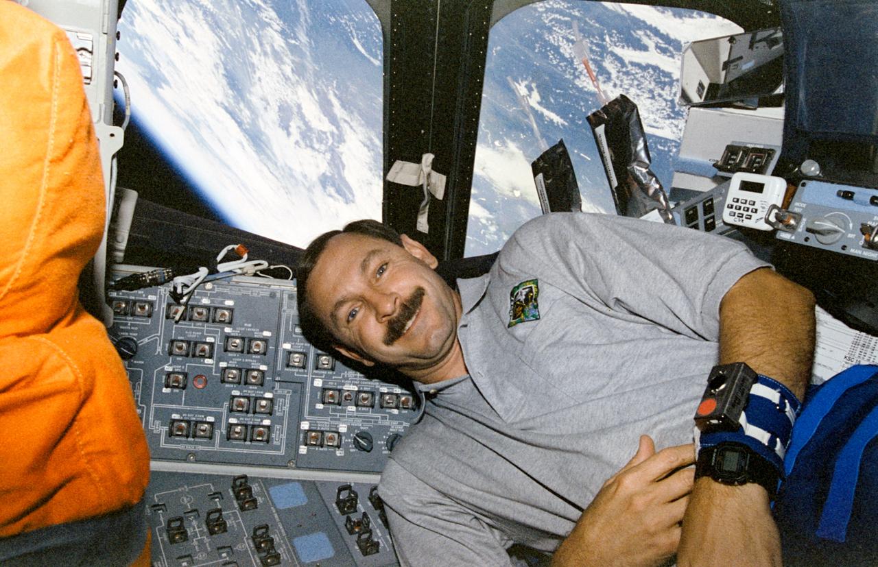 STS085-358-005 (7 - 19 August 1997) --- Astronaut Curtis L. Brown, Jr., mission commander, floats on the flight deck of Space Shuttle Discovery.  The horizon of Earth is visible through the aft flight deck windows.  On Brown's left wrist is a band associated with a Detailed Supplementary Objective (DSO).  Two beverage packets are just beyond the commander's left shoulder.