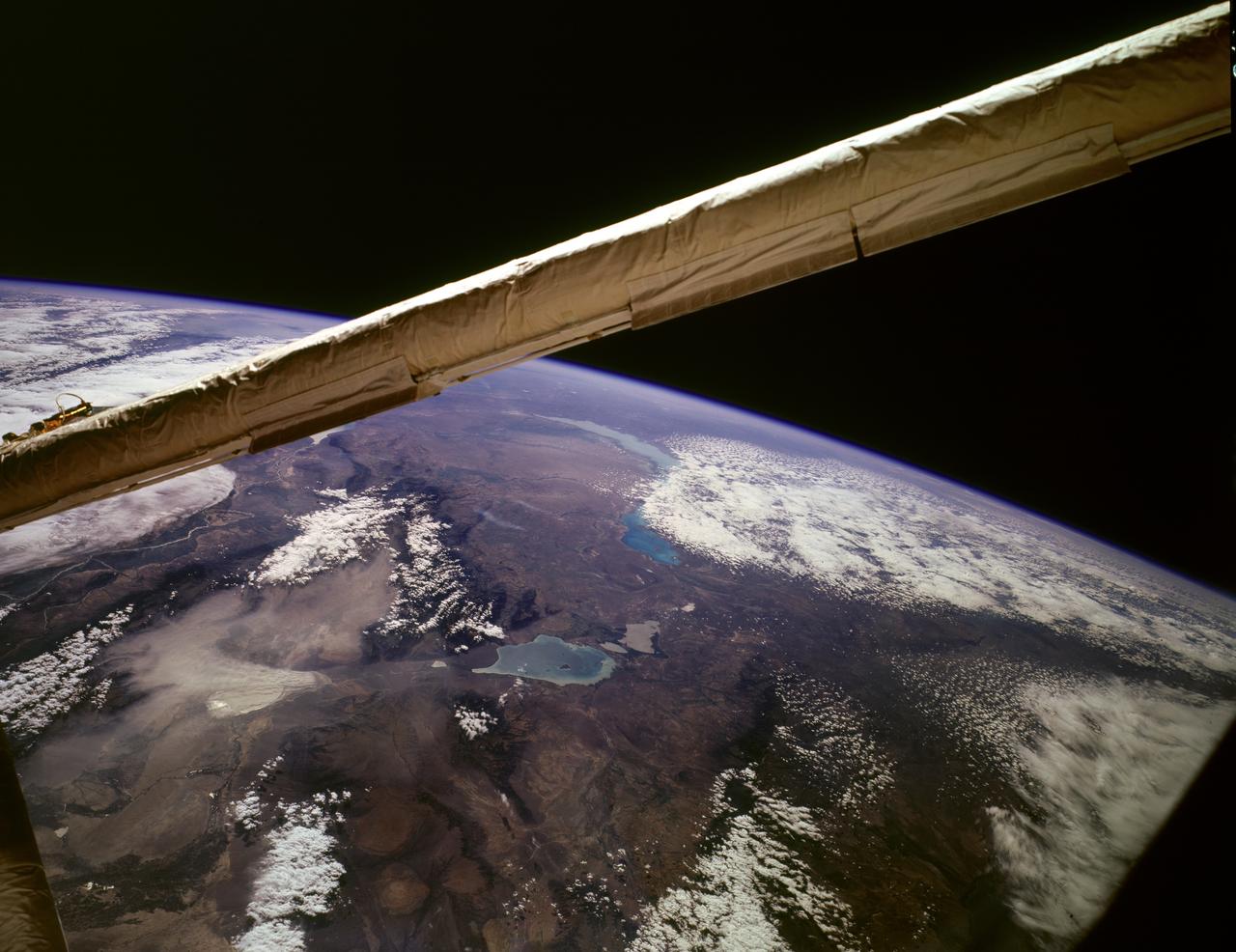 STS085-503-061 (7 - 19 August 1997) --- Lakes Balkhash and Alakol, southern uplands of Kazakhstan, central Asia. The long, 600 kilometers arc of Lake Balkhash occupies the center of this clear west-looking view. The left of the view shows clearly the westernmost Dzungarian Basin in the autonomous region of Xinjiang Uygur (Sinkiang), China. Kazakhstan's capital city Almaty (Alma-Ata) lies out of sight behind the boom. The Dzungarian Gate is the straight, fault-bounded valley cutting through the Dzhungarskiy Alatau Range. The Gate has acted as a major pass for centuries, allowing access between east Asia and central Asia (the valley floor is about 1,500 feet, whereas peaks reach 15,000 feet on the west and about 10,000 feet on the east side) -- it was one of the routes used by the Mongols when they began their invasion of central Asia and Europe in the 13th century. Lake Ebinur is the bright area beneath the dust plume (left center); strong north winds from the steppes of Kazakhstan and Russia are funneled through the Dzungarian Gate where they pick up sediment from dry lakebeds and blow it into China. The Ili River flows westward, parallel to the Dzhungarskiy Alatau Range, through Kapchagay Lake (partially visible beneath boom), then northwest across a large delta plain and into Lake Balkhash.