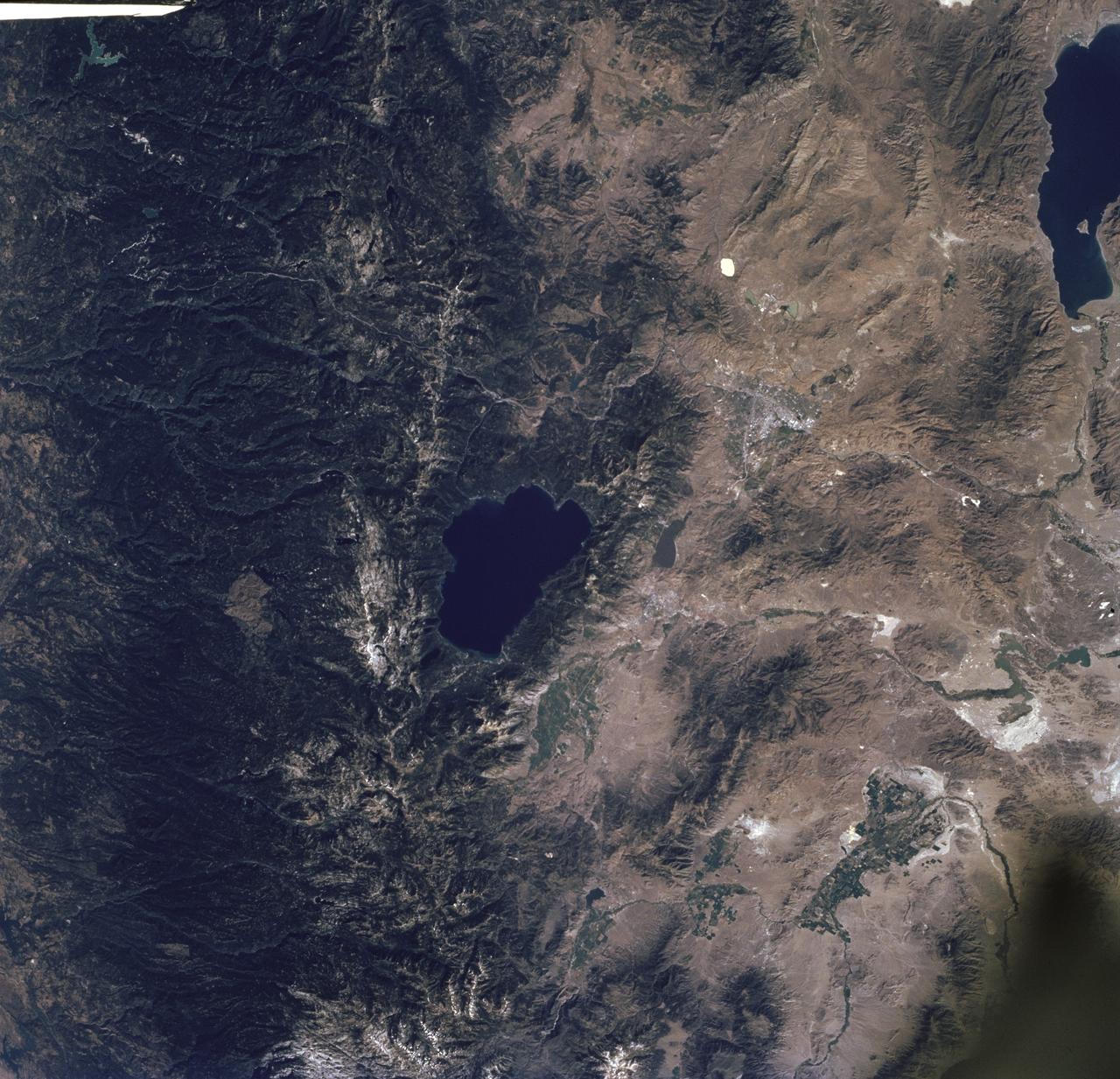 STS085-716-061 (7 - 19 August 1997) --- The dark green forests of the Sierra Nevada Mts. occupy the left side of the picture.  Reno lies between Lake Tahoe (center) and Pyramid Lake (top right).  Lake Tahoe, is a clear, deep alpine lake (over 505 meters deep), surrounded by Montane forest, ski resorts and casinos.  Although Tahoe is known as one of the clearest lakes in the world, water quality in the lake has been declining due to soil erosion from development.  Since 1968, it has lost about 30 feet of clarity.  A partnership was recently formed between environmentalists and resort owners to protect their common interest in keeping the lake as clear as possible.  Over the last five years they have slowed the erosion and the growth of algae that it causes so that clarity is now &quot;only&quot; lost at a rate of roughly one foot per year.  Pyramid Lake (on the upper right of the photo) is as different from Tahoe as a lake could be.  The sagebrush desert around the lake and is owned by the Pyramid Lake Paiute tribe who manage it as a fishery for an endangered sucker (fish), the cui-cui.  The tribe has added modern fisheries' biology methods to their traditional management and chooses not to develop the lake as a recreation destination.  Anaho Island, in the lower half of the lake, is a wildlife refuge managed for American White Pelicans which fly hundreds of miles each day to get from this safe breeding area to the shallow marshes where they feed.  Directly above Lake Tahoe is Donner pass, near the site where the beleaguered Donner Party spent the winter of 1846 - 1847 trapped in the mountains.  Several shallow ephemeral lakes can be seen in Lemmon Valley north of Reno's core urban area.  These lakes would normally have dried up by August when this photo was taken, but are still wet because of the extremely wet winter and floods of January 1997.