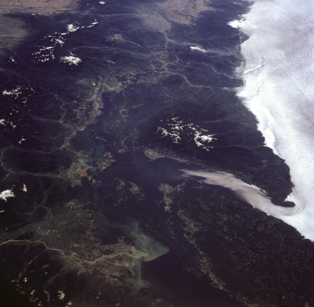 STS085-716-081 (7-19 August 1997) --- This photograph provides a southerly view from Vancouver, B. C. in the foreground, to Portland, Oregon near the top.  Coastal stratus, a common occurrence, hugs the Pacific coastline and laps into Puget sound.  The silty Fraser River cuts through Vancouver and empties into Puget Sound with a large, milky plume of sediment (bottom).  Near the top of the image, the Columbia River runs across the Cascades (between Mt. Adams and Mt. Hood) and the Coast Ranges to the Pacific Ocean.  Snow caps the highest peaks of the Olympic Mountains (near center), and the Cascade volcanoes of Rainier (closest to Seattle), Adams and Hood (top).  The smaller, gray mountain just south (above and right) of Rainier is Mt. St. Helens.