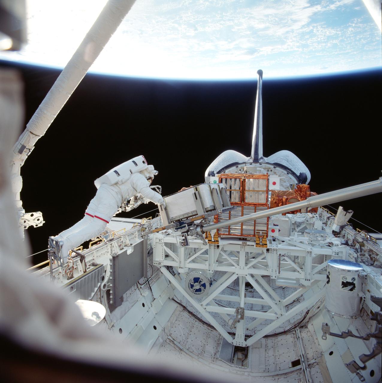 STS087-718-073 (19 November ? 5 December 1997) --- On the Space Shuttle Columbia's first ever spacewalk (EVA), astronaut Winston E. Scott works with a simulated battery and 156-pound crane carried onboard for the first time this trip of Columbia.  The crane's inclusion and the work with it are part of a continuing preparation effort for future work on the International Space Station (ISS).  The ongoing project allows for evaluation of tools and operating methods to be applied to the construction of the ISS.  This crane device is designed to aid future spacewalkers in transporting Orbital Replacement Units (ORU), with a mass up to 600 pounds (like the simulated battery pictured here), from translating carts on the exterior of ISS to various worksites on the truss structure.  Earlier, astronauts Takao Doi (at the base of the crane, out of frame at right), an international mission specialist representing Japan, and Winston E. Scott had installed the crane in a socket along the middle port side of Columbia's cargo bay for the evaluation.  The two began the crane operations, long ago manifest for this mission, after completing a contingency spacewalk to snag the free-flying Spartan 201 and berth it in the payload bay (visible in the background).