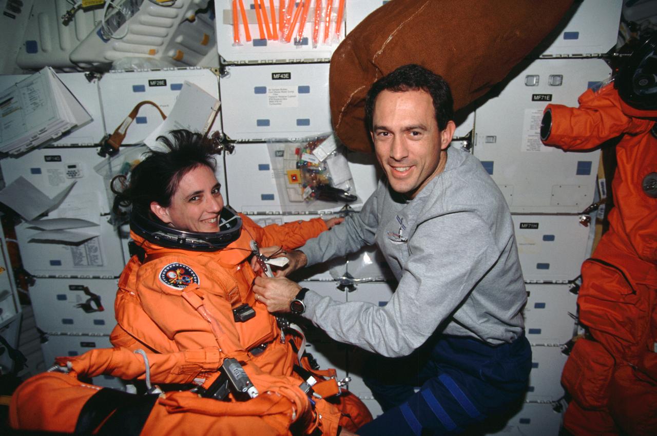 STS088-313-030 (4-15 December 1998) --- Astronaut James H. Newman assists astronaut Nancy J. Currie, both mission specialists, with her launch and entry suit (LES) on the middeck of the Earth-orbiting Space Shuttle Endeavour.  The burnt-orange colored suits are high altitude, partial-pressure garments worn by each crew member for ascent and entry phases of the shuttle flights.