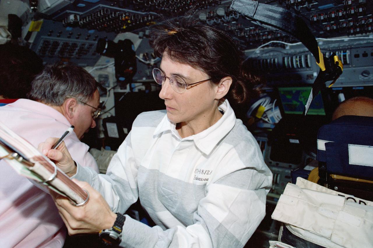 STS088-335-031 (4-15 Dec. 1998) --- Astronaut Nancy J. Currie, mission specialist, makes a notation in a log book on Endeavour's flight deck as astronaut Jerry L. Ross, mission specialist, eyes a control display near the commander's station.  The two were joined by a Russian cosmonaut and three NASA astronauts for eleven days in Earth orbit, spending the majority of their time and efforts in support of important initial links to the International Space Station (ISS).