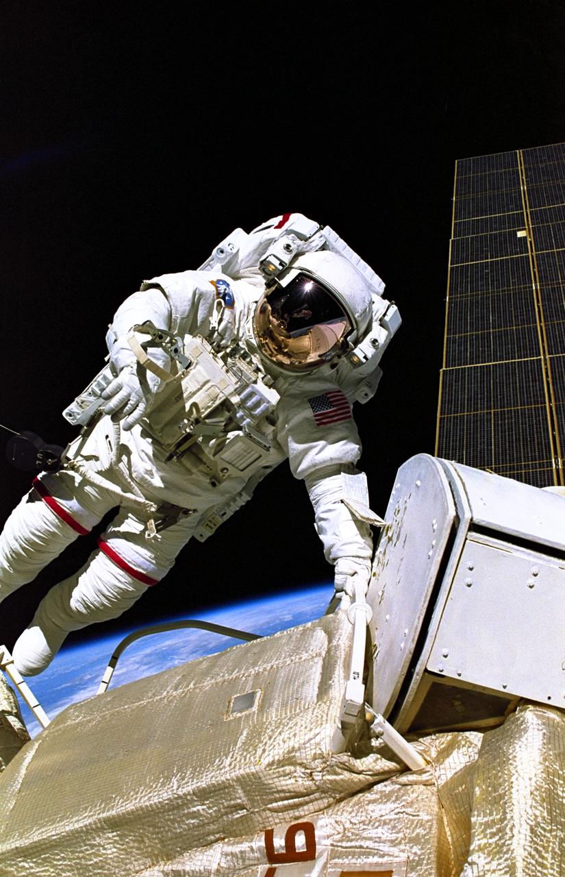 STS088-355-015 (4-15 Dec. 1998) --- Astronaut Jerry L. Ross, STS-88 mission specialist, is pictured during one of three space walks which were conducted on the eleven-day mission.  Perched on the end of Endeavour's remote manipulator system (RMS) arm, astronaut James H. Newman, mission specialist, recorded this image.  Newman can be seen reflected in Ross' helmet visor.  The solar array panel for the Russian-built Zarya module can be seen along right edge.