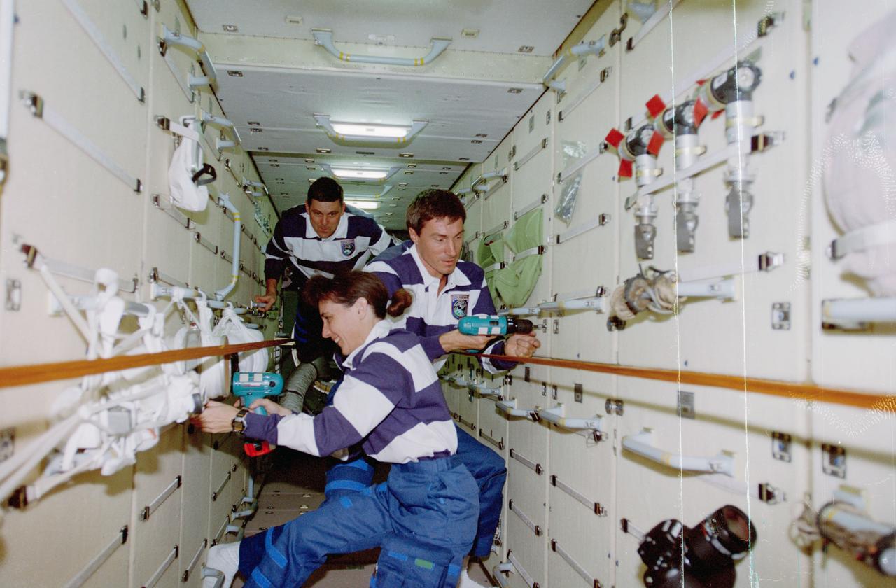 STS088-359-037 (4-15 Dec. 1998) --- Astronaut Nancy J. Currie and cosmonaut Sergei K. Krikalev, both mission specialists, use rechargeable power tools to manipulate nuts and bolts on the Russian-built Zarya module. Astronaut Robert D. Cabana, mission commander, translates along the rail network in the background. The six STS-88 crew members had earlier entered the module through the U.S.-built Unity connecting module. Rails, straps and tools indicate the crewmembers had been working awhile when this photo was taken. Krikalev, representing the Russian Space Agency (RSA), has been assigned as a member of the three-man initial International Space Station (ISS) crew.