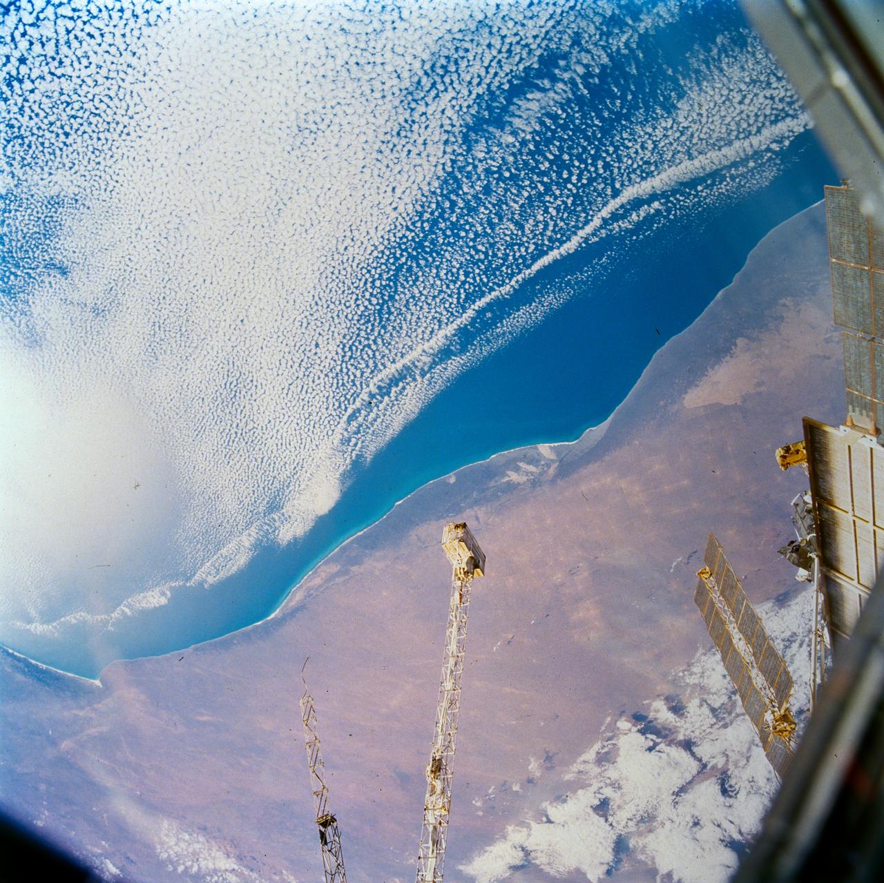 STS089-703-007 (22-32 Jan. 1998) --- This picture of southern Australia was photographed with a 70mm handheld camera from the Earth-orbiting space shuttle Endeavour.  The Nullarbor Plain (behind the boom of Russia’s Mir Space Station) has been one of the least photographed features of the continents.  The coastal escarpment rises abruptly to 500 feet above sea level. The limestone bedrock has been dissolved away along fractures and joints. In this photo of the western Australian Bight, solution grooves can be seen to have localized sand deposits in long bands. Both inland and along the coast, rounded sinkholes and depressions attest to solution of the surficial limestone’s; "karst" is the term for this kind of terrain.  Caves such as Cocklebiddy and Weebubbie are common along the coast and linear passages, formed by dissolution of joints, commonly connect rooms. Photo credit: NASA