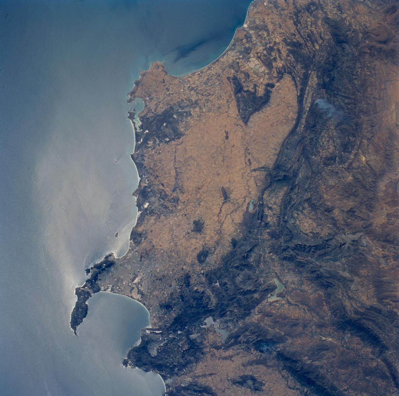 STS089-706-068 (22-31 Jan. 1998) --- This nadir view of the southern Cape District of South Africa was photographed with a 70mm handheld camera from the Earth-orbiting space shuttle Endeavour. Prominent landmarks are the Cape of Good Hope, False Bay and Cape Town. Cape Town is the gray area at the base of the peninsula that forms the Cape of Good Hope. East and north of Cape Town the dark mountain ranges are the Cape Fold Belt. Northerly structures of the region formed approximately 580 million years ago when east Antarctica, Africa and parts of South America combined. According to NASA scientists those continents separated and then recombined about 230 million years ago; in the later event, the northerly structures were again active and the west-trending folds of the Great and Little Karroo ranges formed. The westerly structures of the Karroo formed somewhat later; the northerly structures were re-folded at that time. The great continental mass, Gondwana, remained together until around 175 million years ago, when it rifted apart leaving the coastline essentially as it is seen today. Photos such as this are useful to geologists working in these areas as they provide, quite literally, the big picture in complex regions. Other items of interest are the internal waves noted offshore, several trains can be seen east, north and south of Cape Town. In the mountains to the north (upper left corner) a large brush fire is seen from the smoke plume. The giant gold and diamond mines are located northeast and east of this photo. The gold province is primarily located around Johannesburg (450 miles northeast) and the diamond mines are approximately 300 miles northeast around Kimberley. Photo credit: NASA