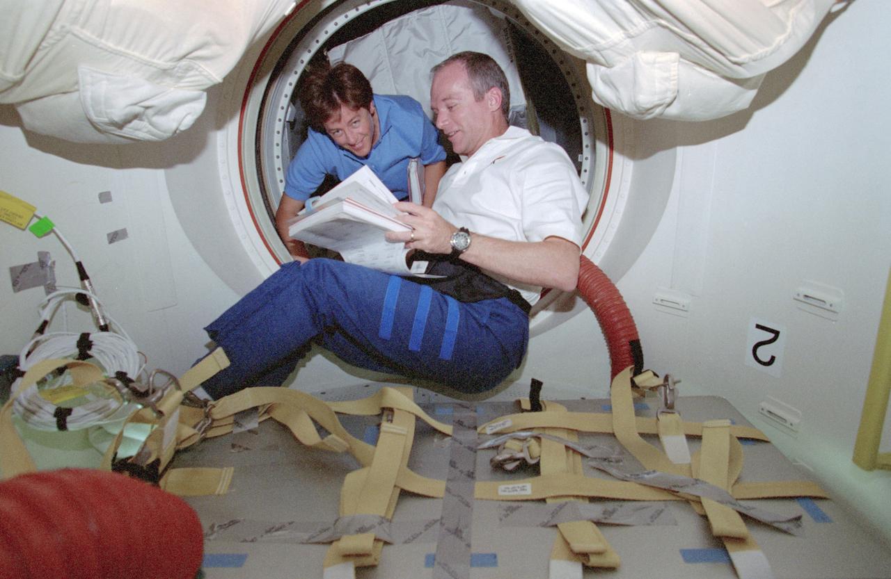 STS091-358-011 (2-12 June 1998) --- In Discovery's airlock, astronauts Charles J. Precourt, mission commander, and Wendy B. Lawrence, mission specialist, look over a copy of the flight plan.  The two were accompanied by three other astronauts and a Russian cosmonaut on a mission to link with Russia's Mir space station for the final time and to retrieve astronaut Andrew S.W. Thomas for return to Earth.